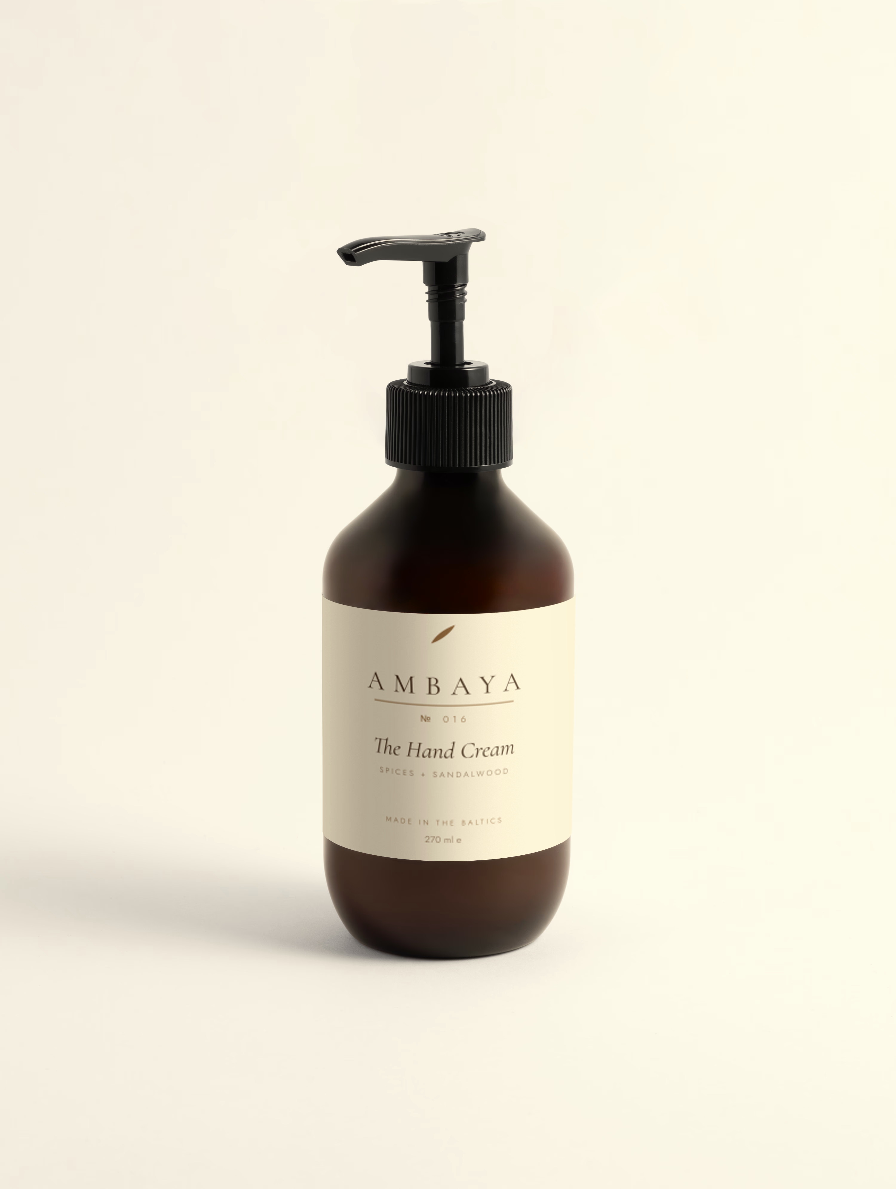 Amber glass bottle of The Hand Cream, 270 ml, with a black pump and cream label carrying the gold AMBAYA wordmark, on a pale cream background.